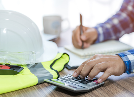 An accountant for a construction company is at a desk using a calculator and writing notes for an audit or review.
