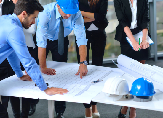 Construction managers considering wip schedule while looking over their plans at a construction site.