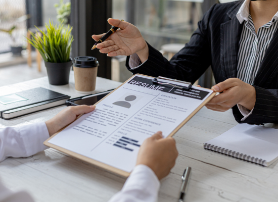 A HR professional is reviewing a resume with a candidate while sitting across from the candidate at an office desk - squared off,.