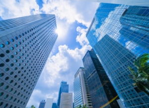 Skyscrapers with reflective glass windows rise against a backdrop of a bright blue sky with scattered clouds.