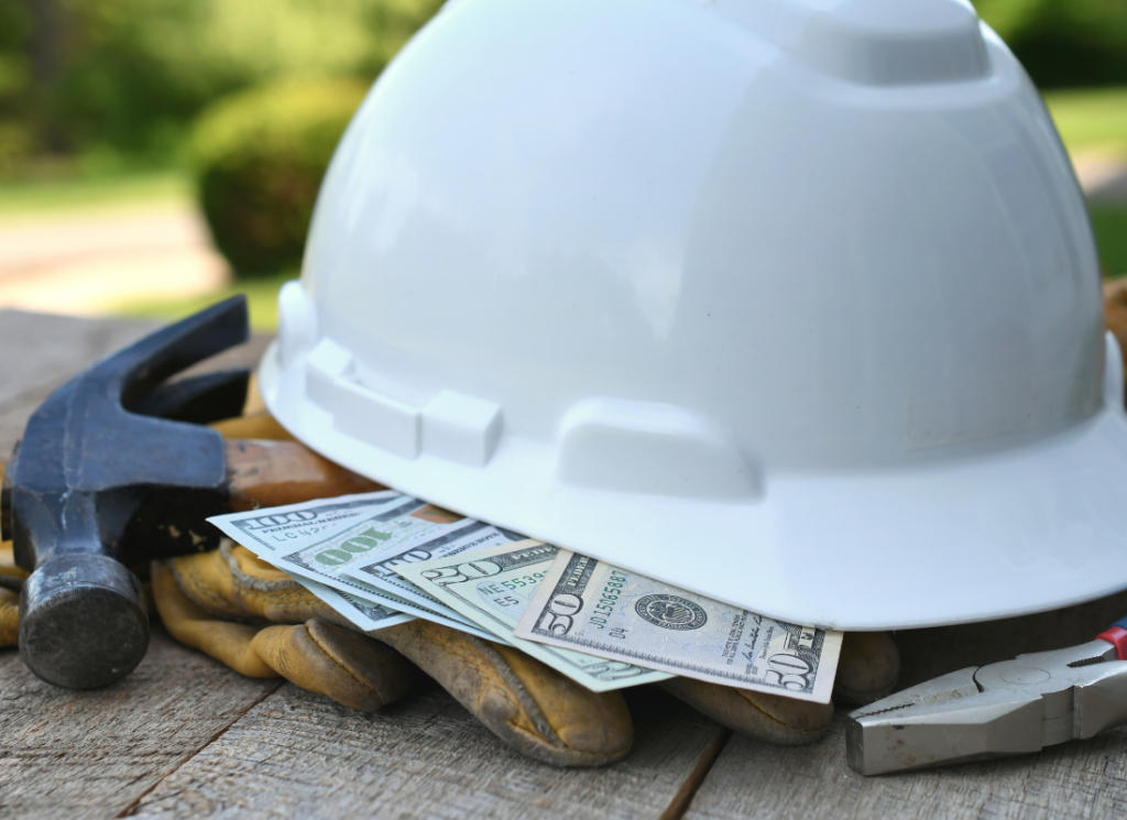 Construction hard hat and tools with cash underneath, symbolizing proactive tax planning for construction company owners.