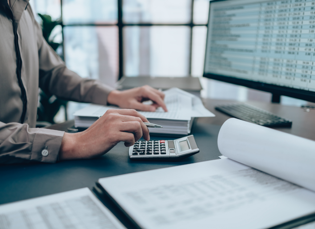 A business tax accountant working at a desk with financial documents, a calculator, and a computer screen, representing year-end tax planning strategies for 2024 business returns.