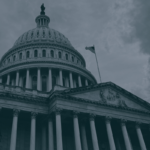 Exterior view of a government building with a large dome, columns, and an American flag flying against a cloudy sky.