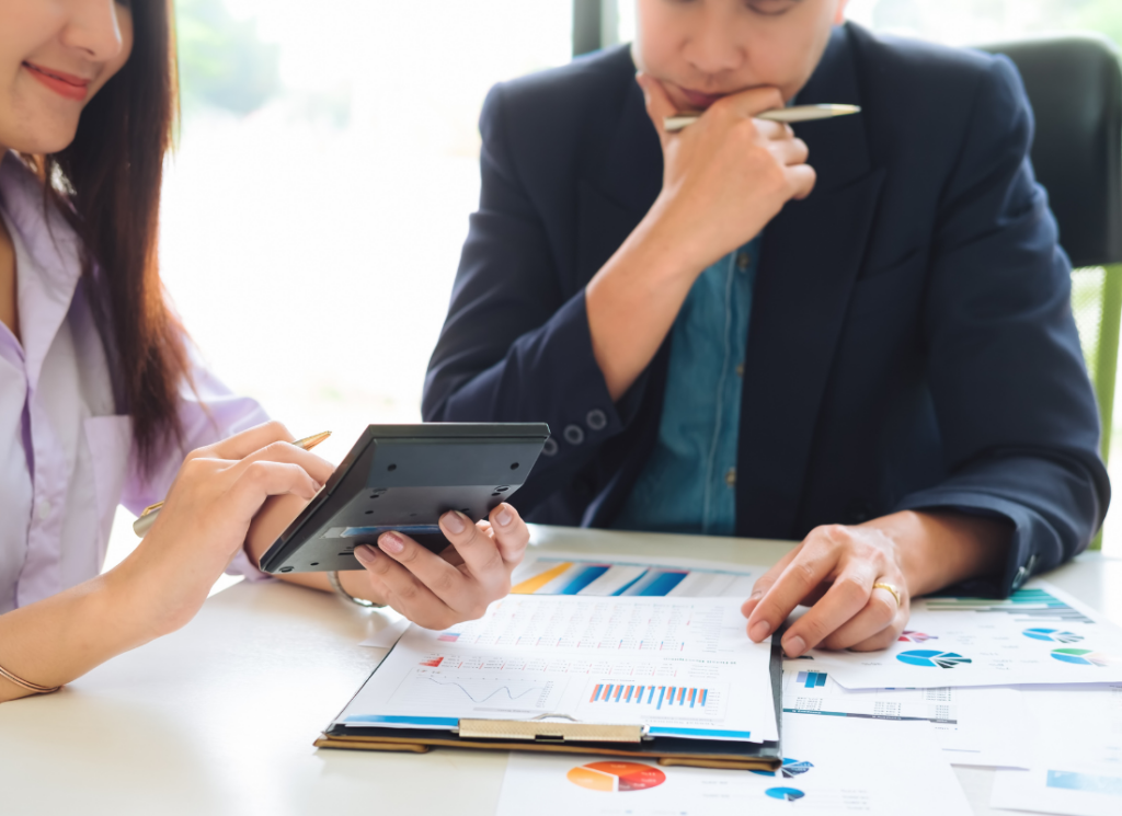 Two nonprofit accountants review financial documents with charts and graphs. One holds a calculator while the other considers data, discussing potential single audit errors.