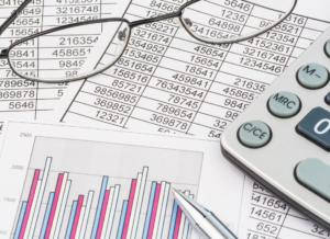 A calculator, glasses, and a pen rest on financial spreadsheets with numerical data and bar graphs, symbolizing analysis, planning, and financial strategy.