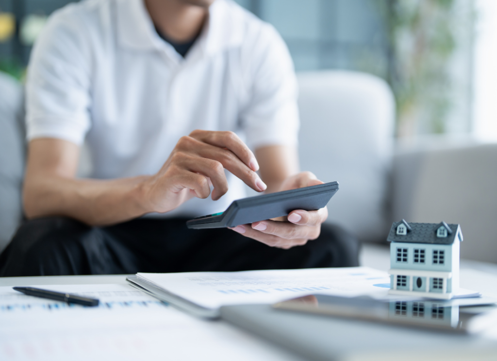 A person uses a calculator at a desk with financial documents and a small model house, symbolizing real estate tax planning and energy-efficient home credit opportunities.