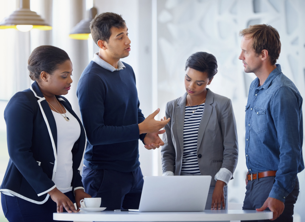 A diverse group of nonprofit professionals gathered around a laptop in a modern office, engaged in a focused discussion—illustrating collaborative outsourced HR support for nonprofits.