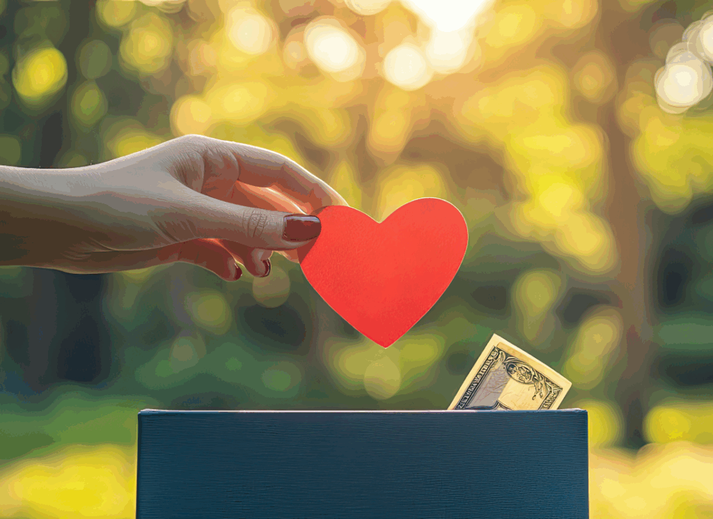 A hand places a red heart into a donation box beside a dollar bill, symbolizing charitable giving and the importance of effective grant management systems for nonprofits.