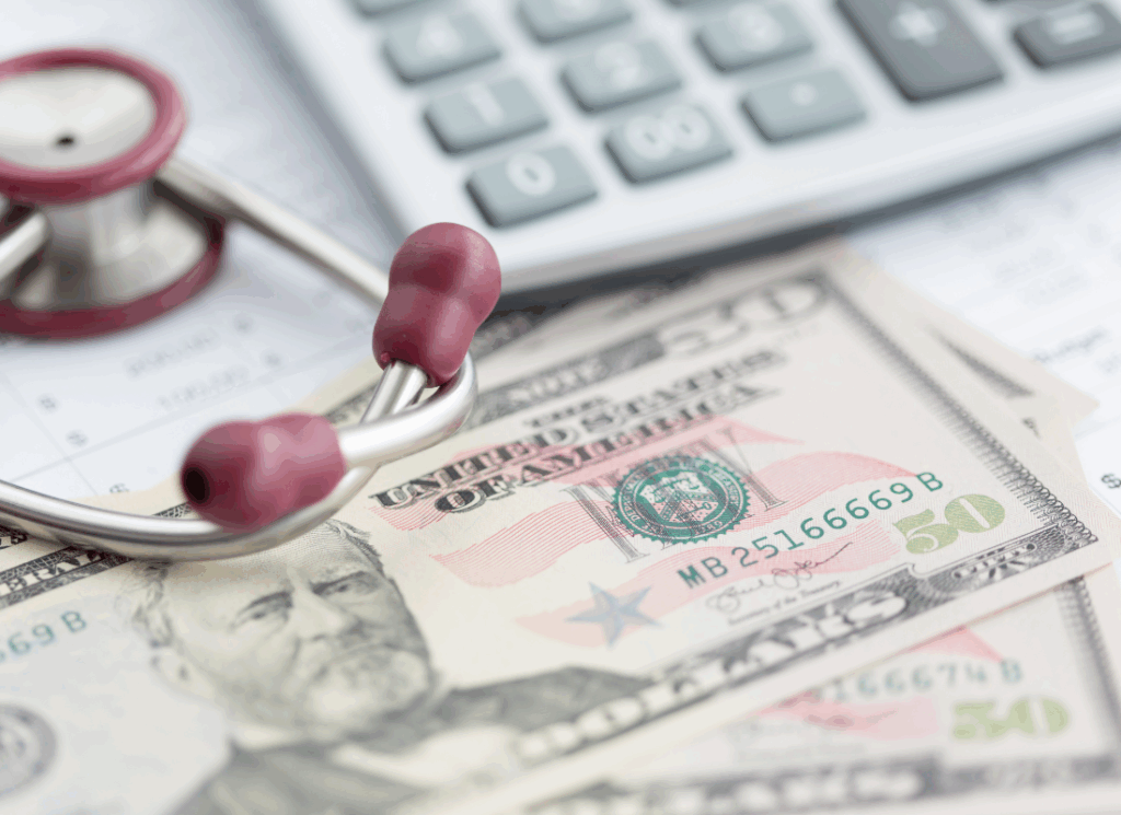 A stethoscope rests on top of U.S. fifty-dollar bills beside a calculator and financial documents, symbolizing healthcare cost accounting for medical practices.