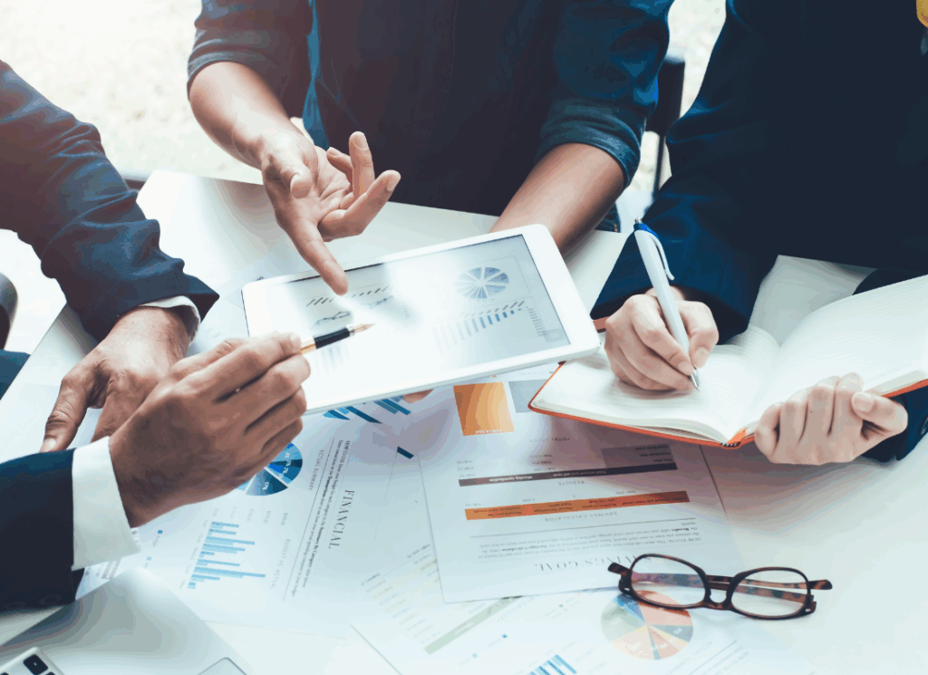 Three property management professionals review financial charts and graphs on paper and a tablet, with one person taking notes, representing accounting for property management companies.