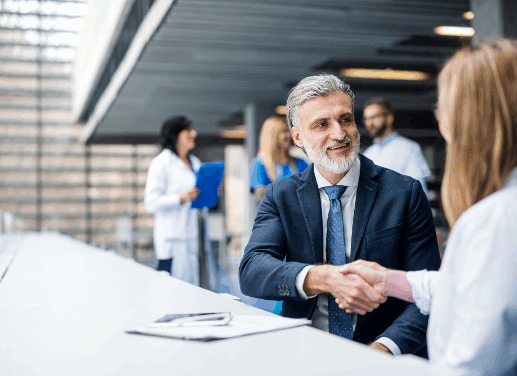A business investor shakes hands with a healthcare worker in a medical facility, symbolizing a partnership and illustrating how to open a clinic without being a doctor.