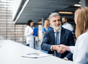 A business investor shakes hands with a healthcare worker in a medical facility, symbolizing a partnership and illustrating how to open a clinic without being a doctor.