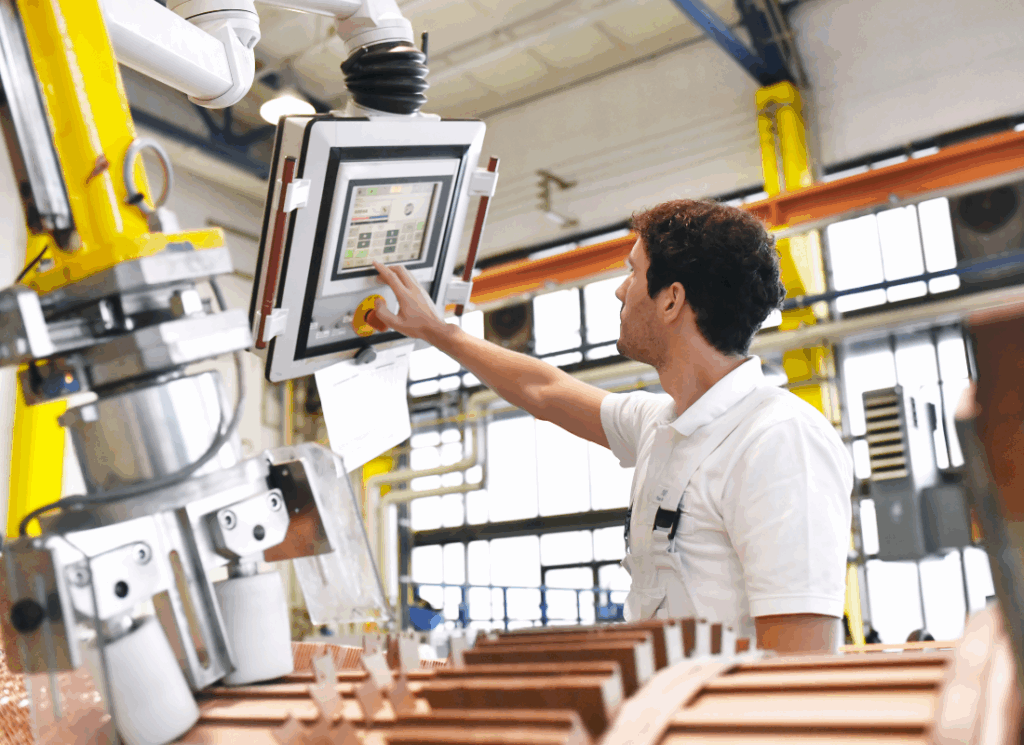 A factory worker operates a touchscreen control panel on industrial equipment inside a manufacturing facility, representing the impact of hidden operational inefficiencies on profitability.