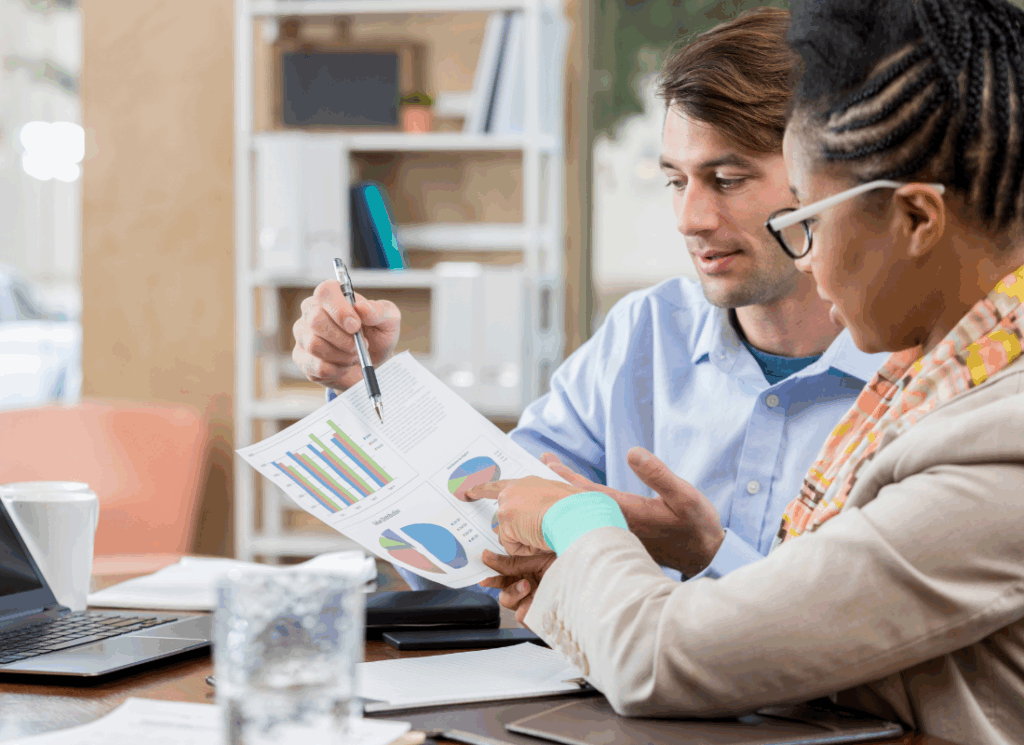Two nonprofit accounting professionals sit at a desk reviewing charts and graphs, discussing financial data, representing collaboration in selecting the best not-for-profit accounting partner.