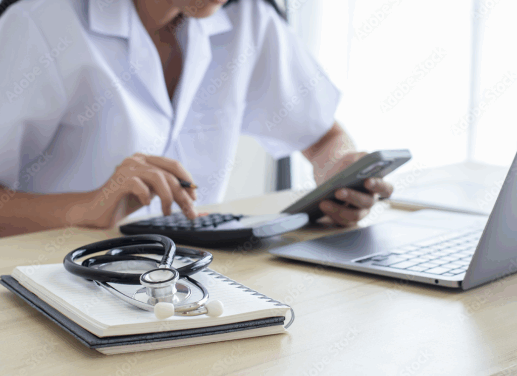 A healthcare professional uses a calculator and smartphone at a desk with a stethoscope and laptop, symbolizing the One Big Beautiful Bill Act healthcare impact on accounting and tax planning.