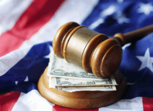 A wooden gavel rests on top of U.S. dollar bills and an American flag. This image represents the financial and tax impact of The One Big Beautiful Bill.