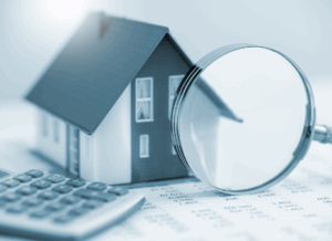 A miniature house model sits next to a magnifying glass and calculator on top of a financial spreadsheet, symbolizing analysis and accounting real estate investment accounting.