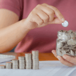 A person stacks coins in ascending order next to a jar filled with change, symbolizing financial planning and charitable giving under the OBBBA tax provisions.