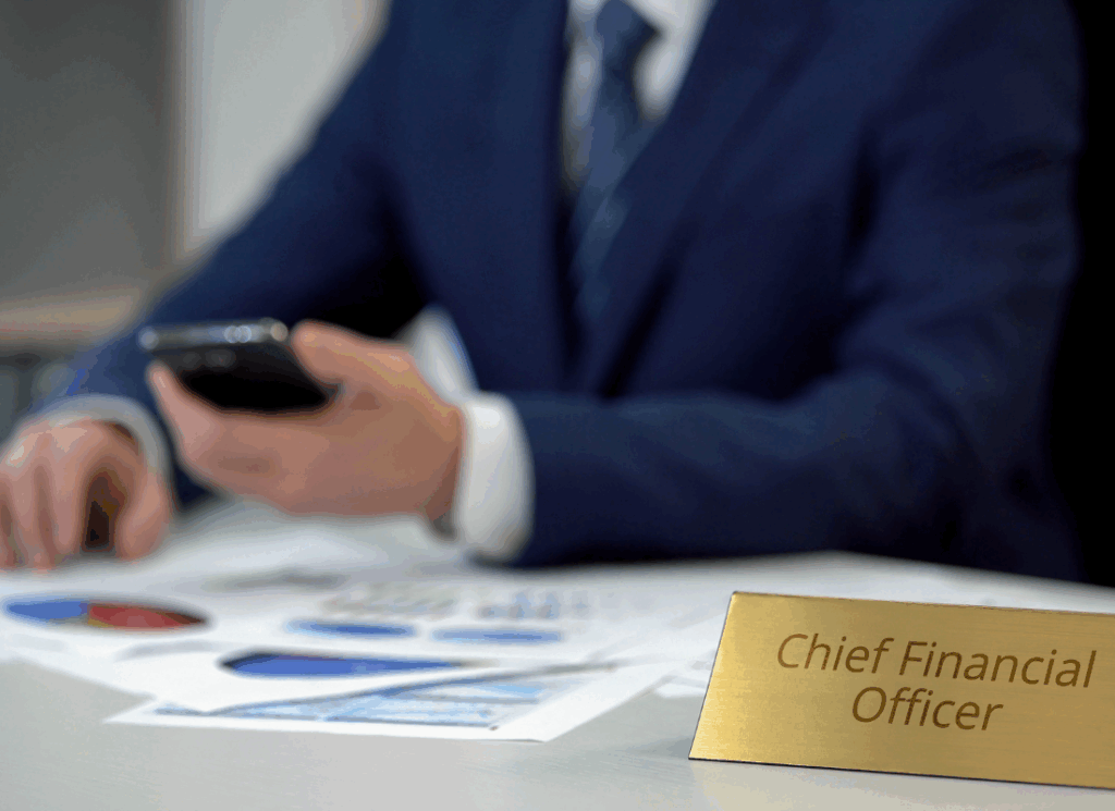 A person in a business suit reviews financial charts while holding a smartphone, with a nameplate reading “Chief Financial Officer,” symbolizing modern CFO skills in higher education.