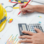 A construction accountant calculates financial data with a pencil and calculator on top of construction-related charts and graphs, next to a yellow hard hat, symbolizing construction bookkeeping.