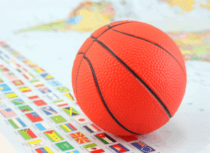 A bright orange basketball sits on top of a map filled with international flags, to represent revenue sharing for international student-athletes.
