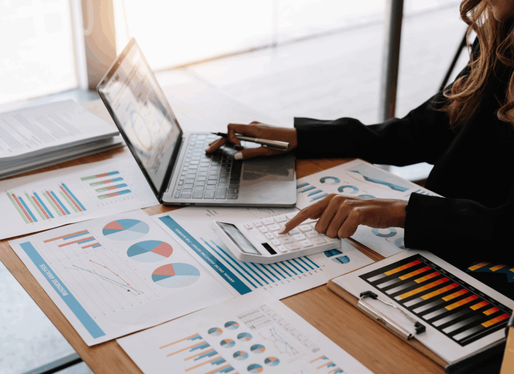 A business professional reviews graphs and financial documents while using a calculator and laptop, representing analysis of SALT cap increase, PTET, and OBBBA implications for business owners.