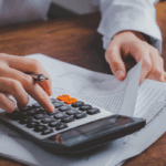 An individual uses a calculator on top of tax documents, holding a pen and reviewing a 1040 form, representing updates to the standard deduction and child tax credit under the One Big Beautiful Bill Act.