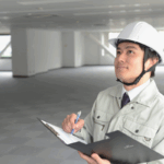 A construction professional in a hard hat reviews notes on a clipboard inside a building, symbolizing bookkeeping for construction companies.