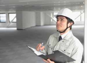 A construction professional in a hard hat reviews notes on a clipboard inside a building, symbolizing bookkeeping for construction companies.