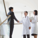 A businessman shakes hands with a doctor while another stands nearby, symbolizing a non-physician owned medical practice.