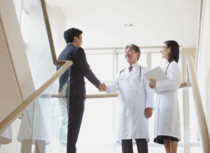 A businessman shakes hands with a doctor while another stands nearby, symbolizing a non-physician owned medical practice.