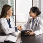Two female doctors smiling and shaking hands in an office, and collaborating on starting a medical practice.