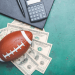 A football on top of dollar bills with a calculator and pen, symbolizing financial concerns and tax risks in collegiate athletics.