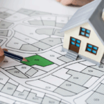 A hand points to a plot on a zoning map beside a small house model, symbolizing LIHTC and NMTC changes after the OBBBA.