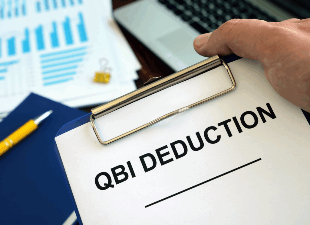 A clipboard labeled QBI Deduction with financial charts in the background, symbolizing the QBI deduction under the OBBBA.