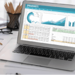 A laptop displaying financial spreadsheets sits on a desk with construction plans and a hard hat, symbolizing construction bookkeeping services.