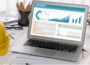 A laptop displaying financial spreadsheets sits on a desk with construction plans and a hard hat, symbolizing construction bookkeeping services.