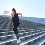 A woman runs up wide outdoor steps at a college sports stadium, representing the SCORE vs. SAFE Act impact on college athletics.