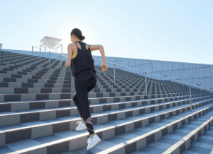 A woman runs up wide outdoor steps at a college sports stadium, representing the SCORE vs. SAFE Act impact on college athletics.