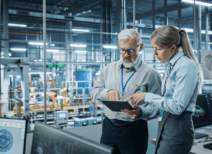 Two professionals in a manufacturing facility review data on a tablet, representing sales and use tax compliance in multi-state operations.