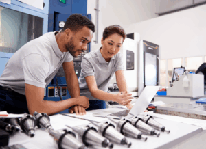 Two manufacturing professionals review data on a laptop beside metal parts, illustrating sales tax exemption for manufacturing operations.