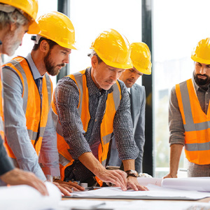 Transition-Planning A construction project manager at a desk reviewing blueprints side-by-side with financial reports on a laptop/tablet.