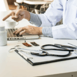 A doctor reviews medical records and financial documents on a laptop with a stethoscope and medications on the desk, illustrating the importance of accounting for doctors.
