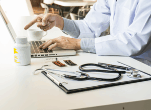 A doctor reviews medical records and financial documents on a laptop with a stethoscope and medications on the desk, illustrating the importance of accounting for doctors.