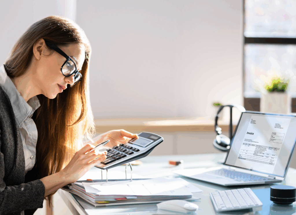 A healthcare accountant reviews financial documents with a calculator and laptop, illustrating accounting for medical practices.