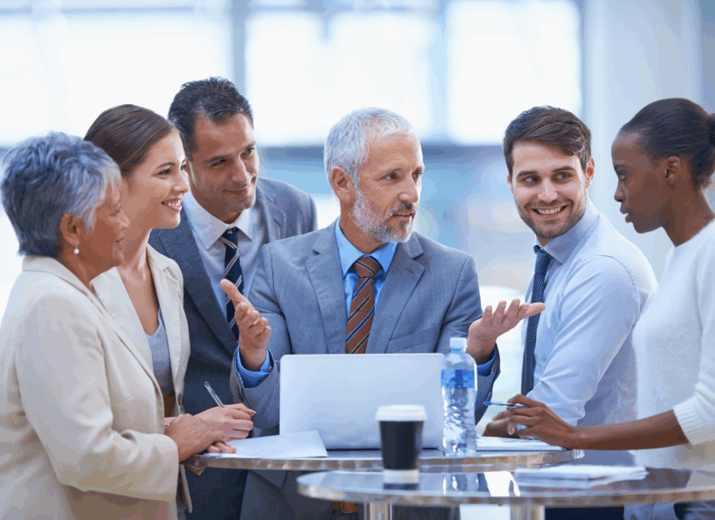 A group of manufacturing business professionals gather around a laptop in discussion, representing collaboration and strong leadership in manufacturing.
