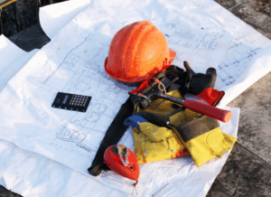 A hard hat, tools, and a calculator sit on top of construction blueprints, representing planning and bonding construction work on a job site.