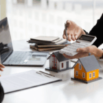 Areal estate CPA reviews numbers beside model houses and a laptop, illustrating guidance on choosing the right structure for real estate family office planning.