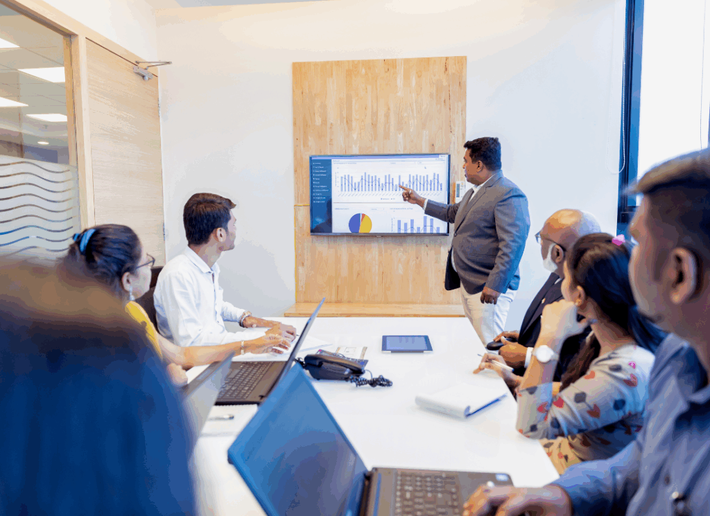 A presenter reviews financial charts with a team in a conference room, illustrating strategic planning and data-driven decision-making for Athletics CFOs.