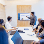 A presenter reviews financial charts with a team in a conference room, illustrating strategic planning and data-driven decision-making for Athletics CFOs.